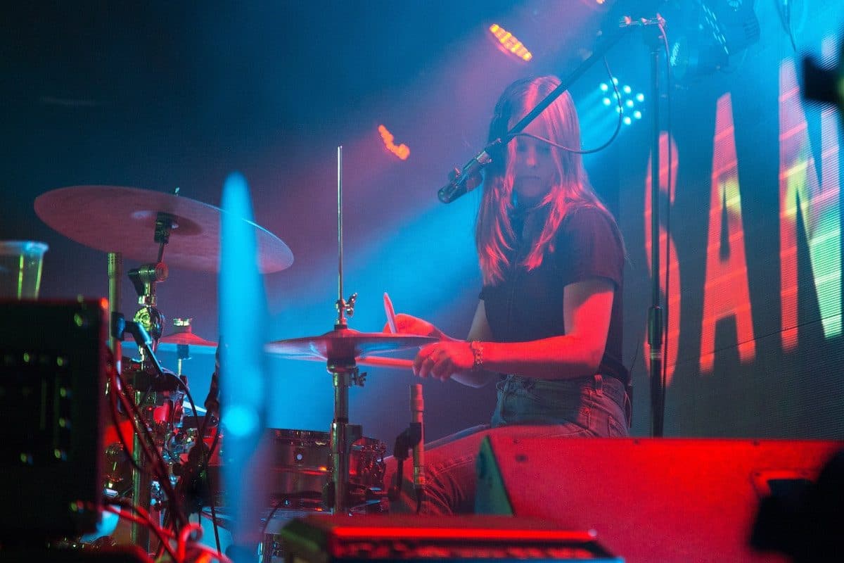 A picture of a girl playing drums at a club in neon light.